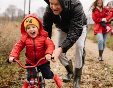 Father helping son ride a bicycle on a fall day while mother and daughter watch.